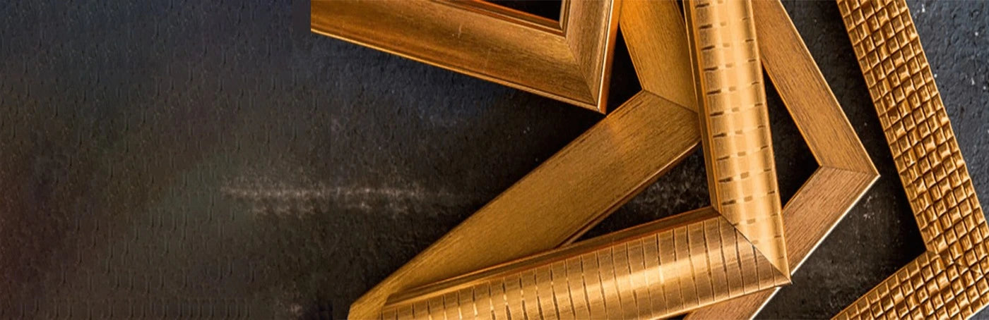 Several unfinished picture frame corners in varying bronze and gold metallic finishes, showcasing different profiles and textures against a dark surface.
